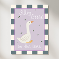 A vertical canvas wall art print featuring a white goose illustration on a lavender background with the words 'Silly Goose on the loose.' The print has a blue-gray and cream checkered border and is shown hanging against a light gray wall.