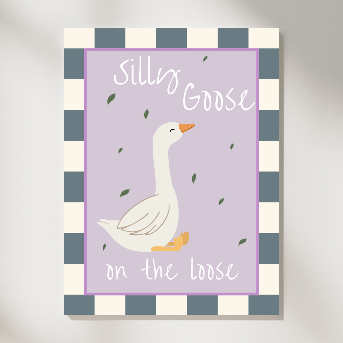A vertical canvas wall art print featuring a white goose illustration on a lavender background with the words 'Silly Goose on the loose.' The print has a blue-gray and cream checkered border and is shown hanging against a light gray wall.