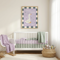 A framed nursery wall art print featuring a white goose on a lavender background with the words 'Silly Goose on the loose,' hung above a white crib in a softly styled nursery with a rocking chair, blanket, basket, and stuffed toys.
